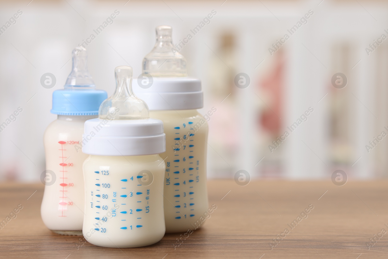 Photo of Feeding bottles with milk on wooden table indoors, space for text