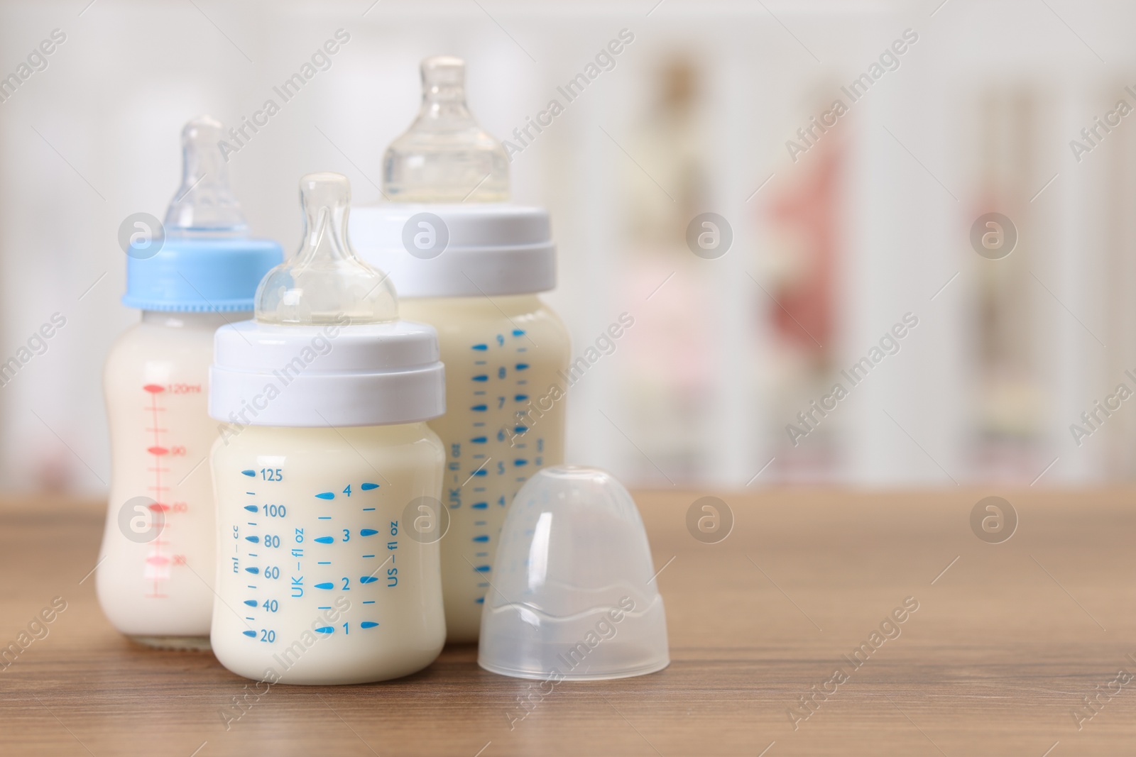 Photo of Feeding bottles with milk on wooden table indoors, space for text