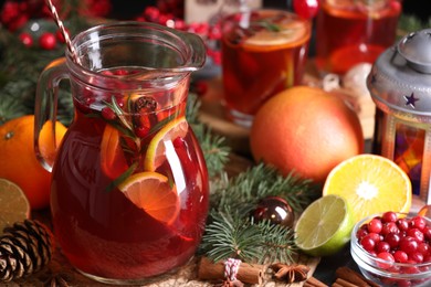 Photo of Tasty punch drink in glass jug, ingredients and Christmas decor on table