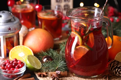 Photo of Tasty punch drink in glass jug, ingredients and Christmas decor on table