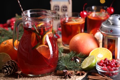 Photo of Tasty punch drink in glass jug, ingredients and Christmas decor on table