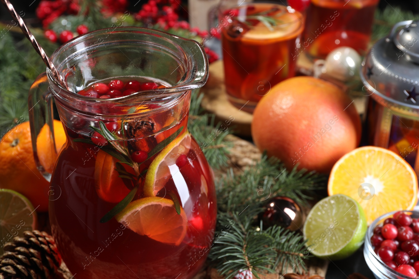 Photo of Tasty punch drink in glass jug, ingredients and Christmas decor on table, closeup