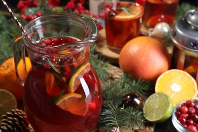 Photo of Tasty punch drink in glass jug, ingredients and Christmas decor on table, closeup