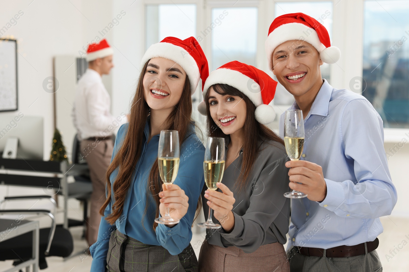 Photo of Cheerful coworkers in Santa hats with glasses of wine at office Christmas party