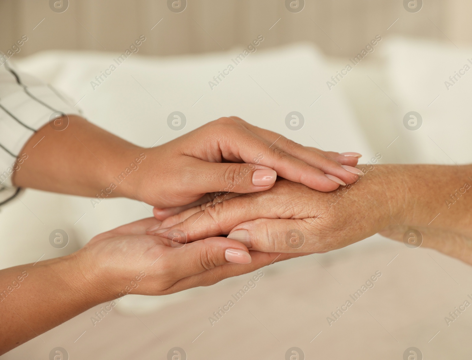 Photo of Young and elderly women holding hands indoors, closeup