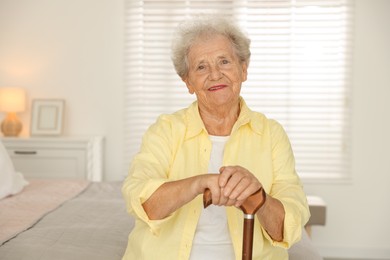 Photo of Senior woman with walking cane sitting on bed at home