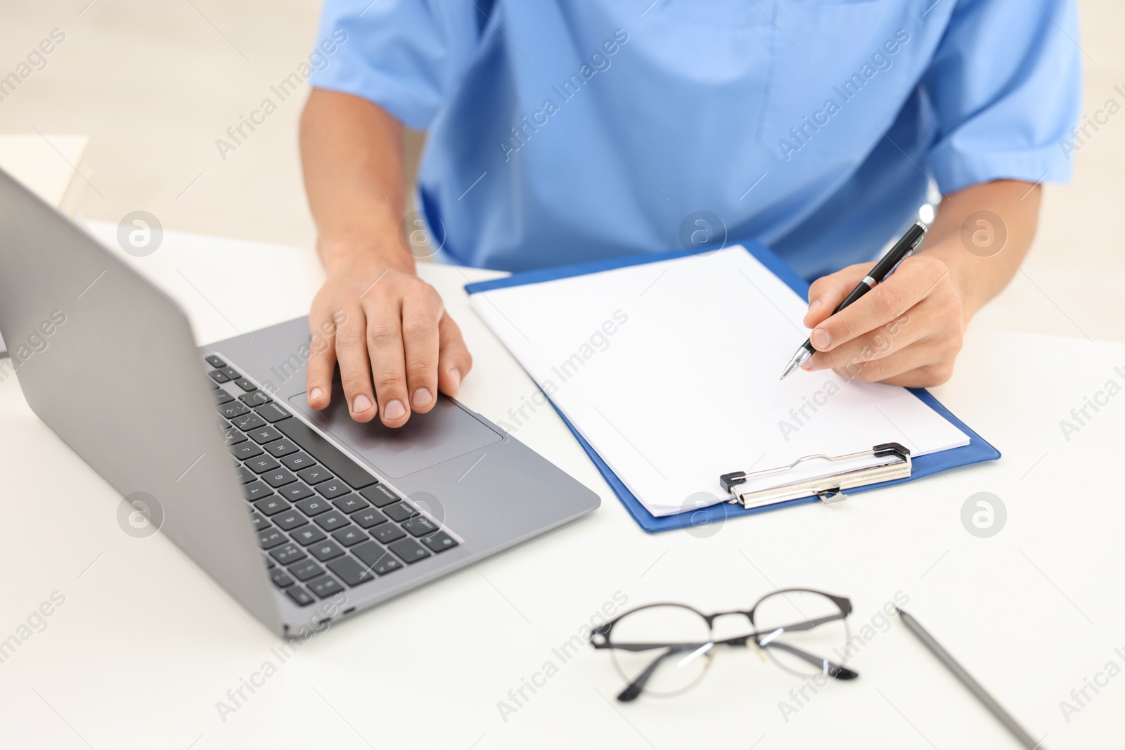 Photo of Medical student taking notes while studying with laptop at table indoors, closeup