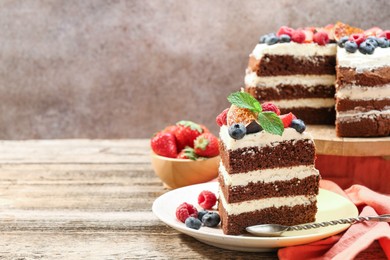 Photo of Piece of delicious chocolate sponge cake with berries served on wooden table, space for text