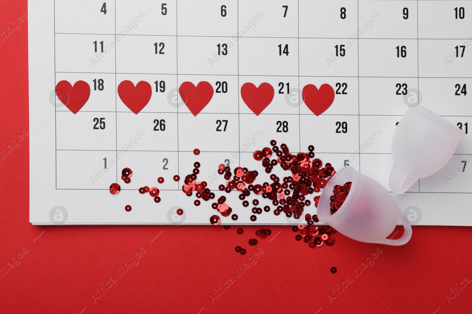 Photo of Calendar with marked dates and menstrual cups on red background, top view