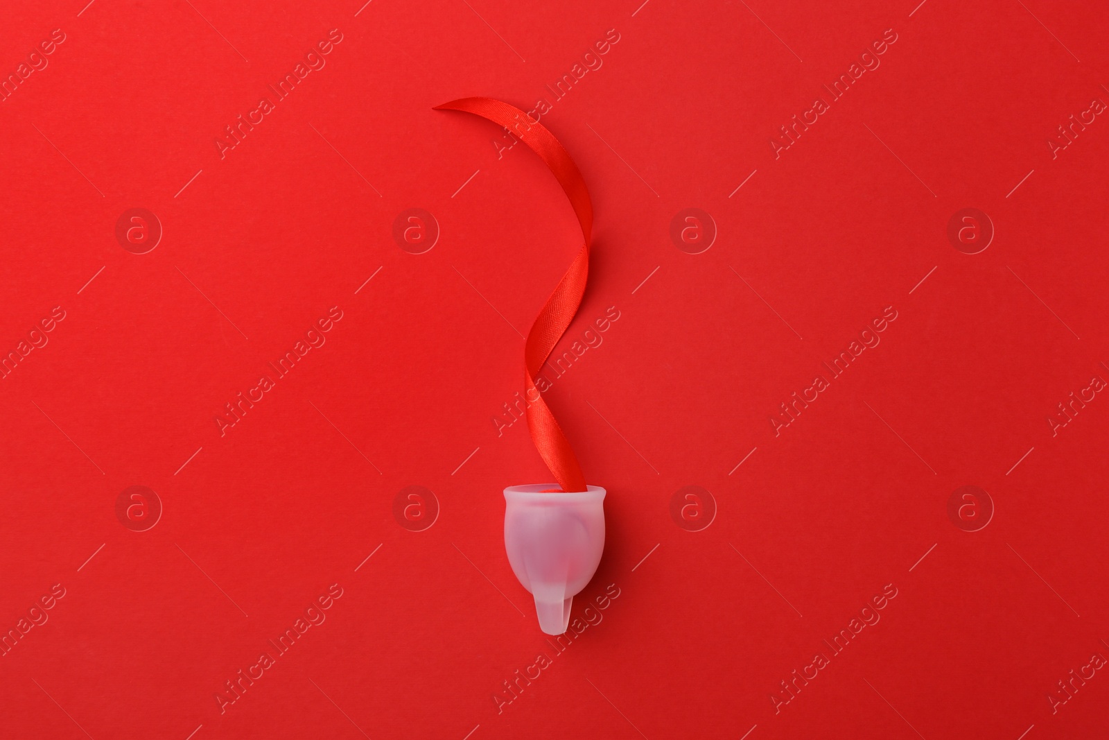 Photo of Menstrual cup with ribbon on red background, top view