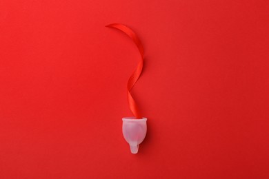 Photo of Menstrual cup with ribbon on red background, top view