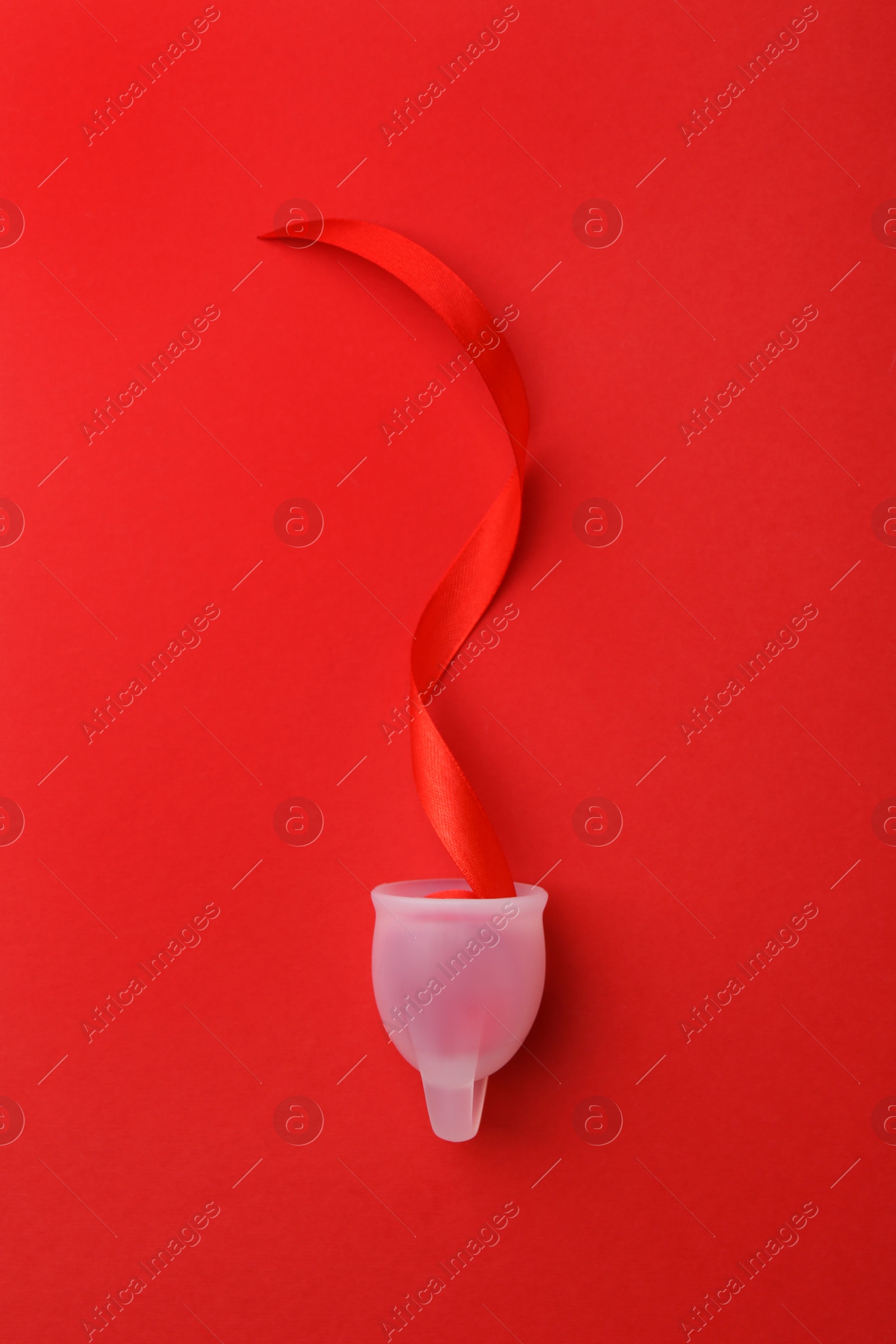 Photo of Menstrual cup with ribbon on red background, top view