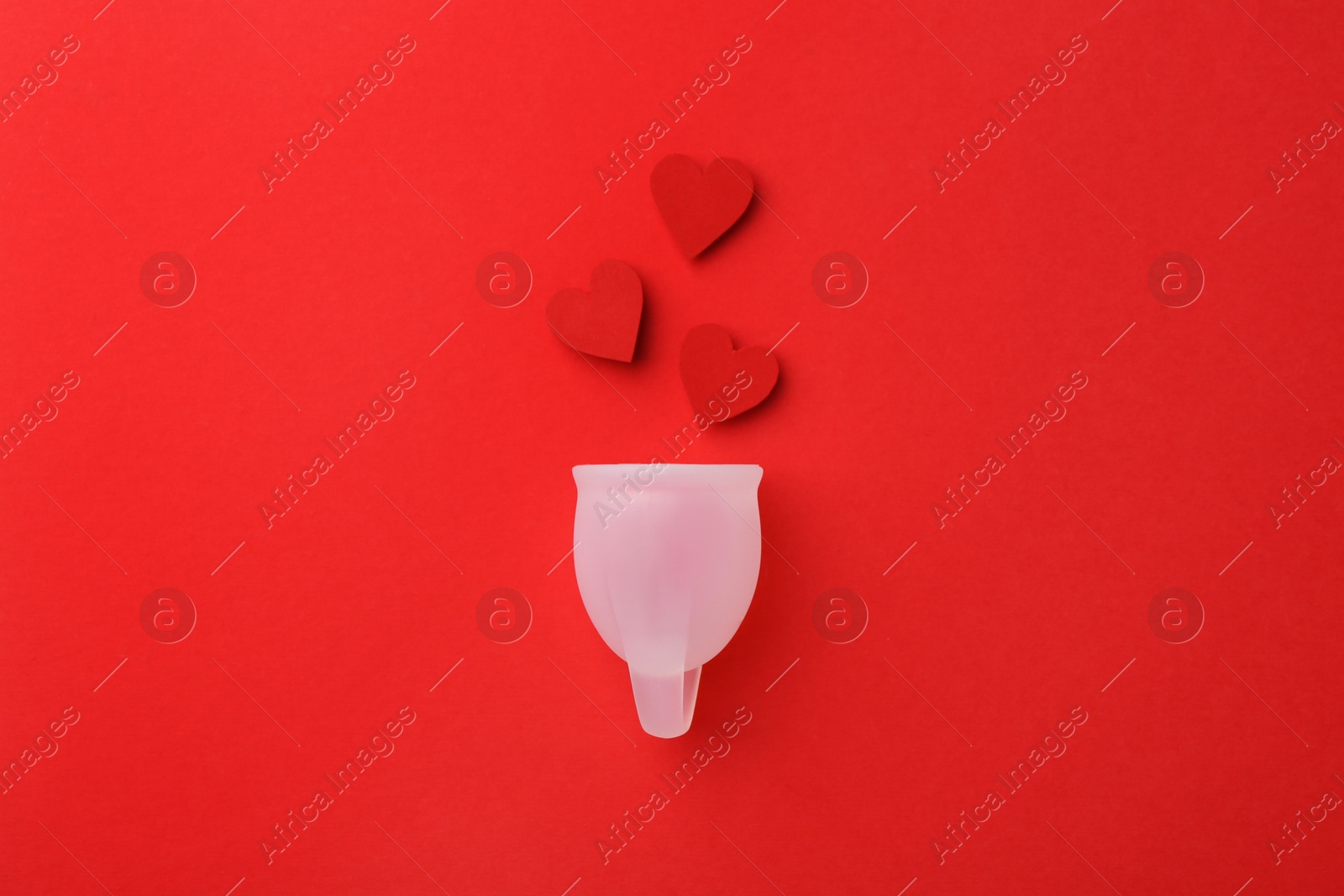 Photo of Menstrual cup with hearts on red background, top view