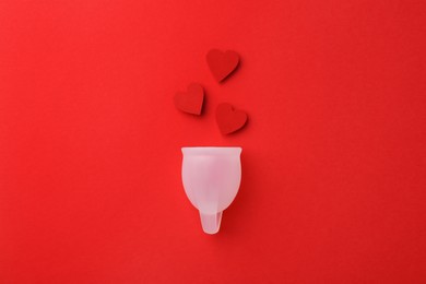 Photo of Menstrual cup with hearts on red background, top view