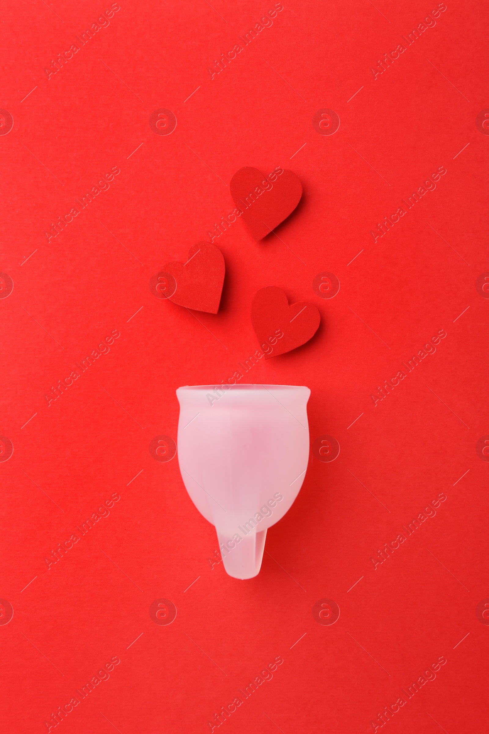 Photo of Menstrual cup with hearts on red background, top view