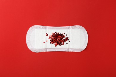 Photo of Menstrual pad with sequins on red background, top view