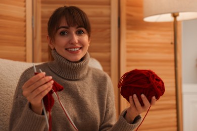 Photo of Beautiful woman knitting with needles in armchair at home