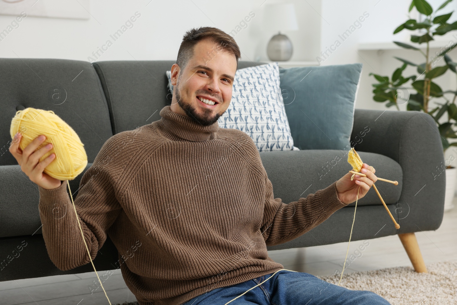 Photo of Man with yellow yarn and knitting needles on floor at home