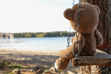 Lonely teddy bear on swing near river, space for text