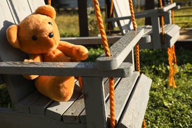 Lonely teddy bear on swing in park