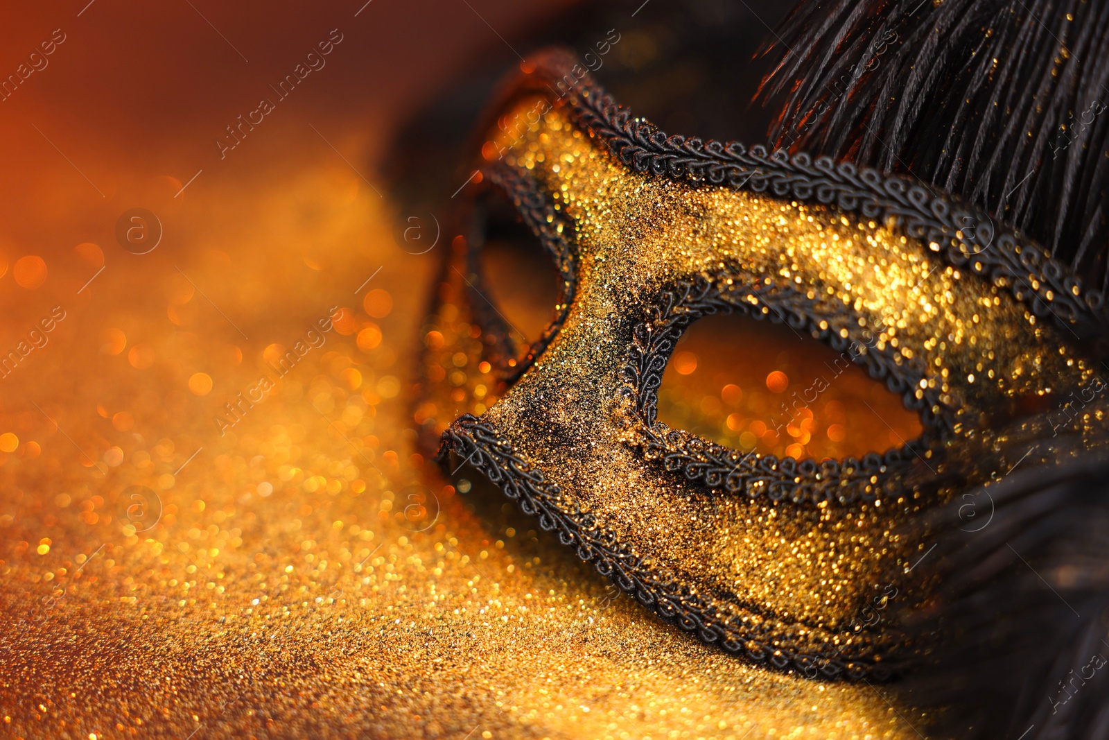 Photo of Beautiful carnival mask and black feathers on glitter background, closeup. Space for text