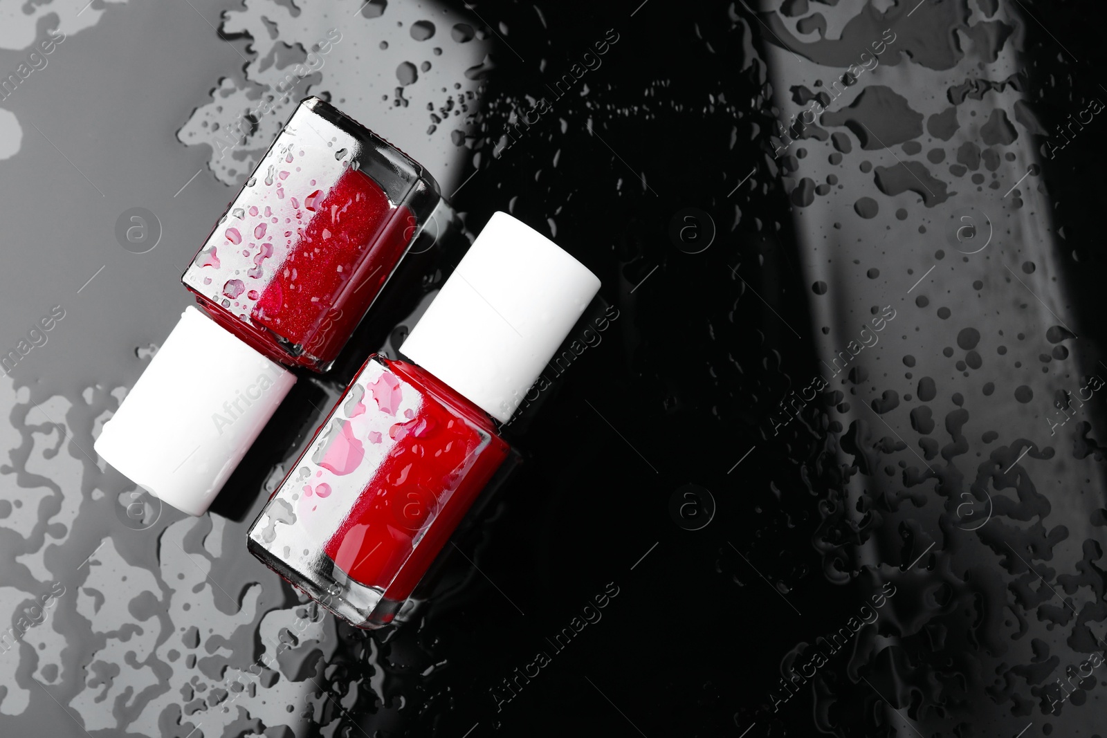 Photo of Nail polishes in bottles on wet dark surface, flat lay. Space for text