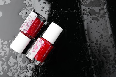 Photo of Nail polishes in bottles on wet dark surface, flat lay. Space for text