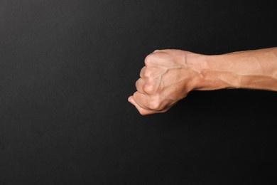 Photo of Man with bulging veins on his arm against black background, closeup. Space for text