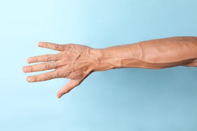 Photo of Man with bulging veins on his arm against light blue background, closeup