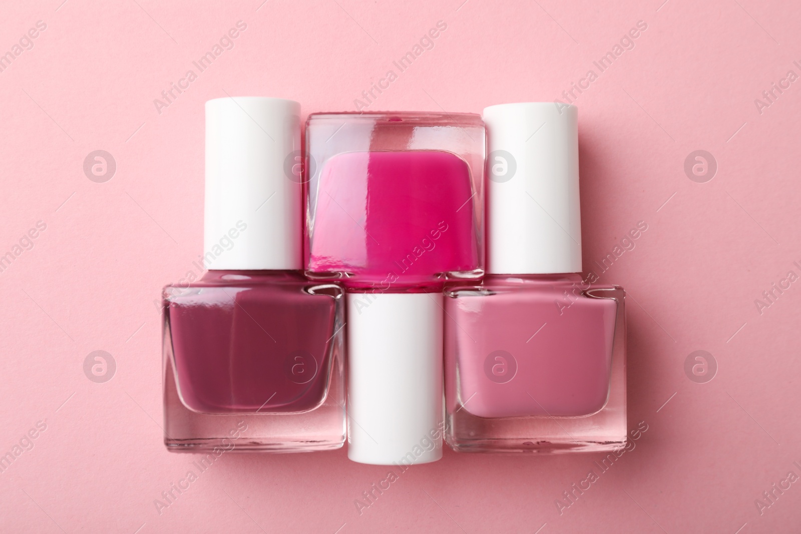 Photo of Set of different nail polishes in bottles on pink background, flat lay