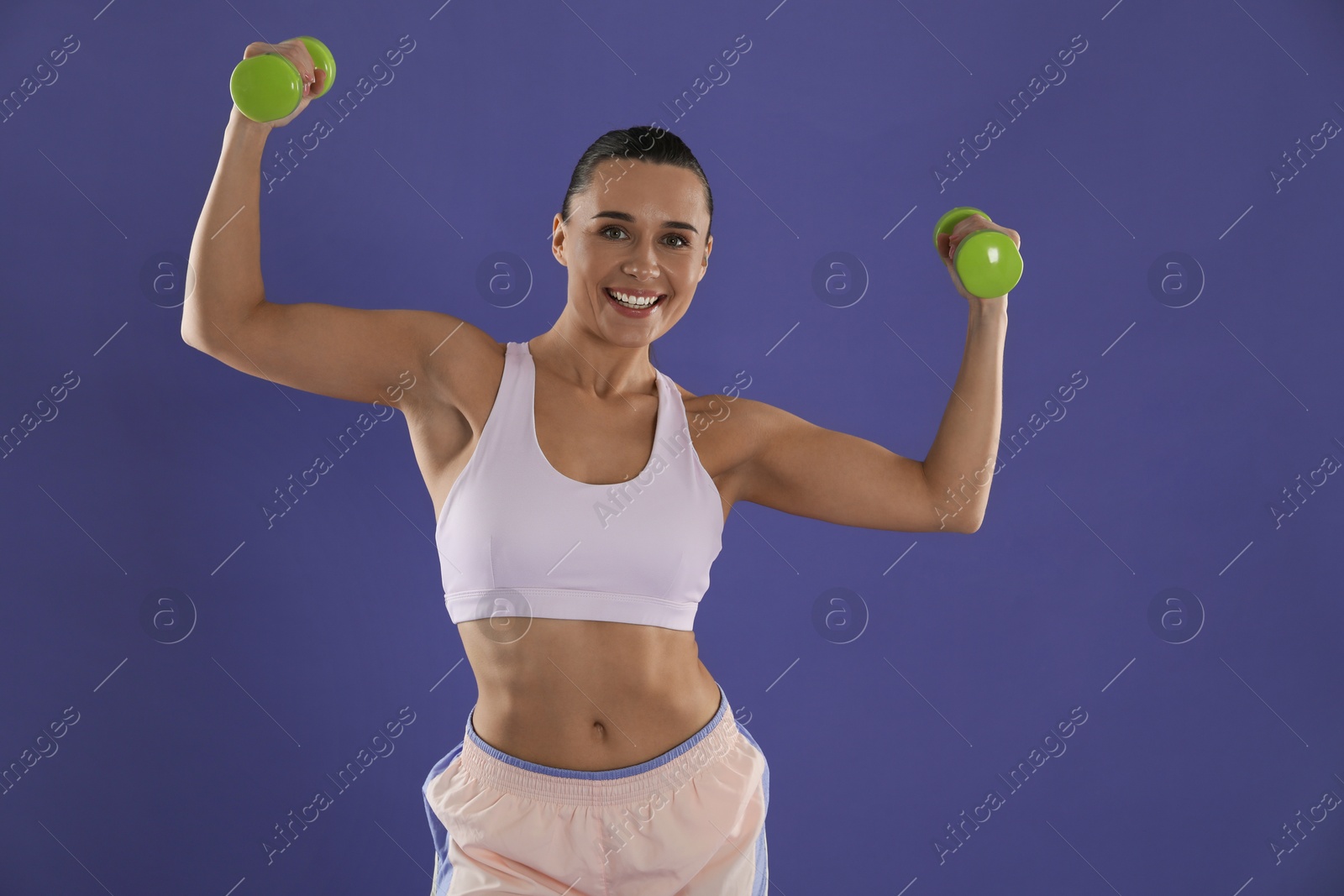 Photo of Woman exercising with dumbbells on purple background