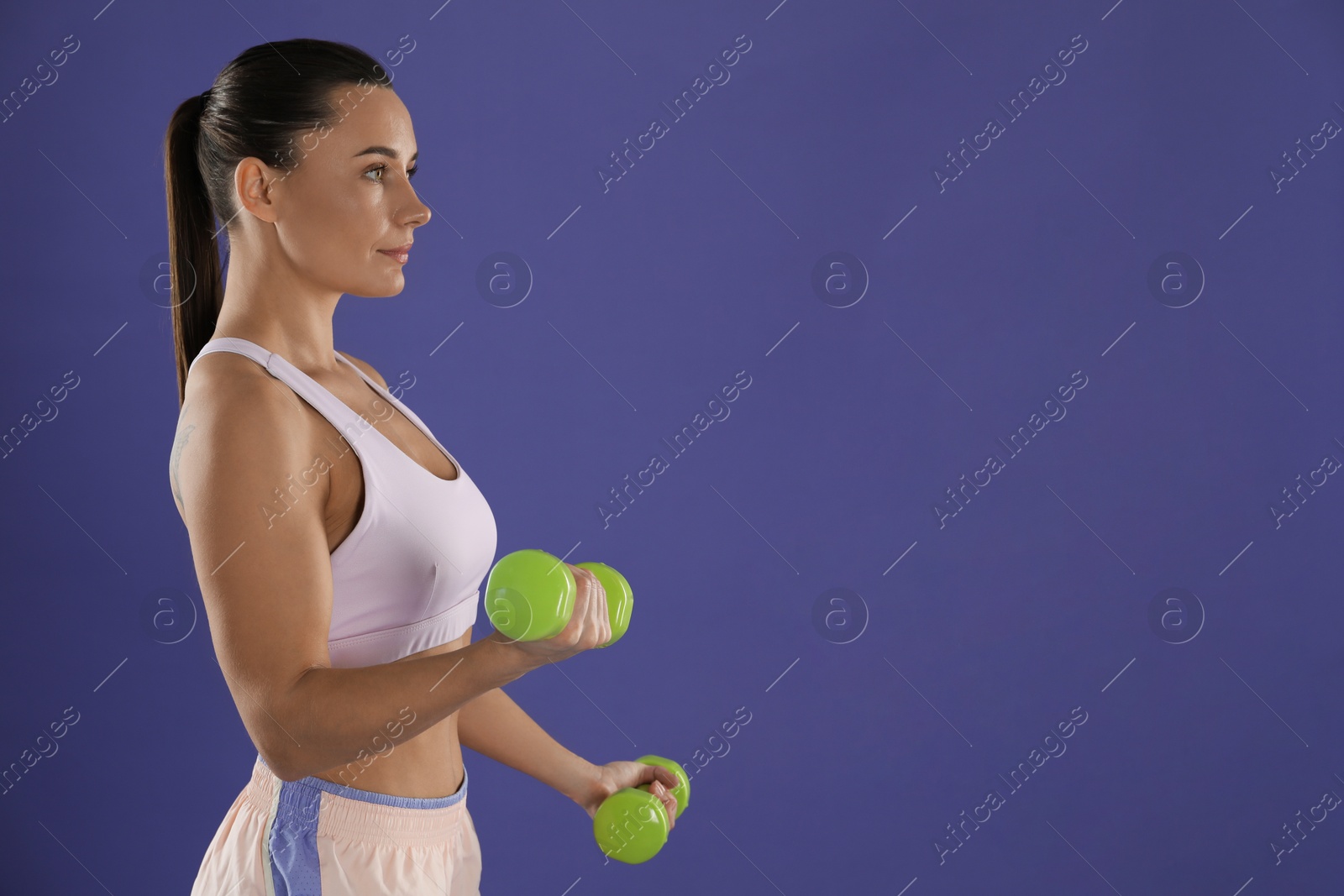 Photo of Woman exercising with dumbbells on purple background, space for text