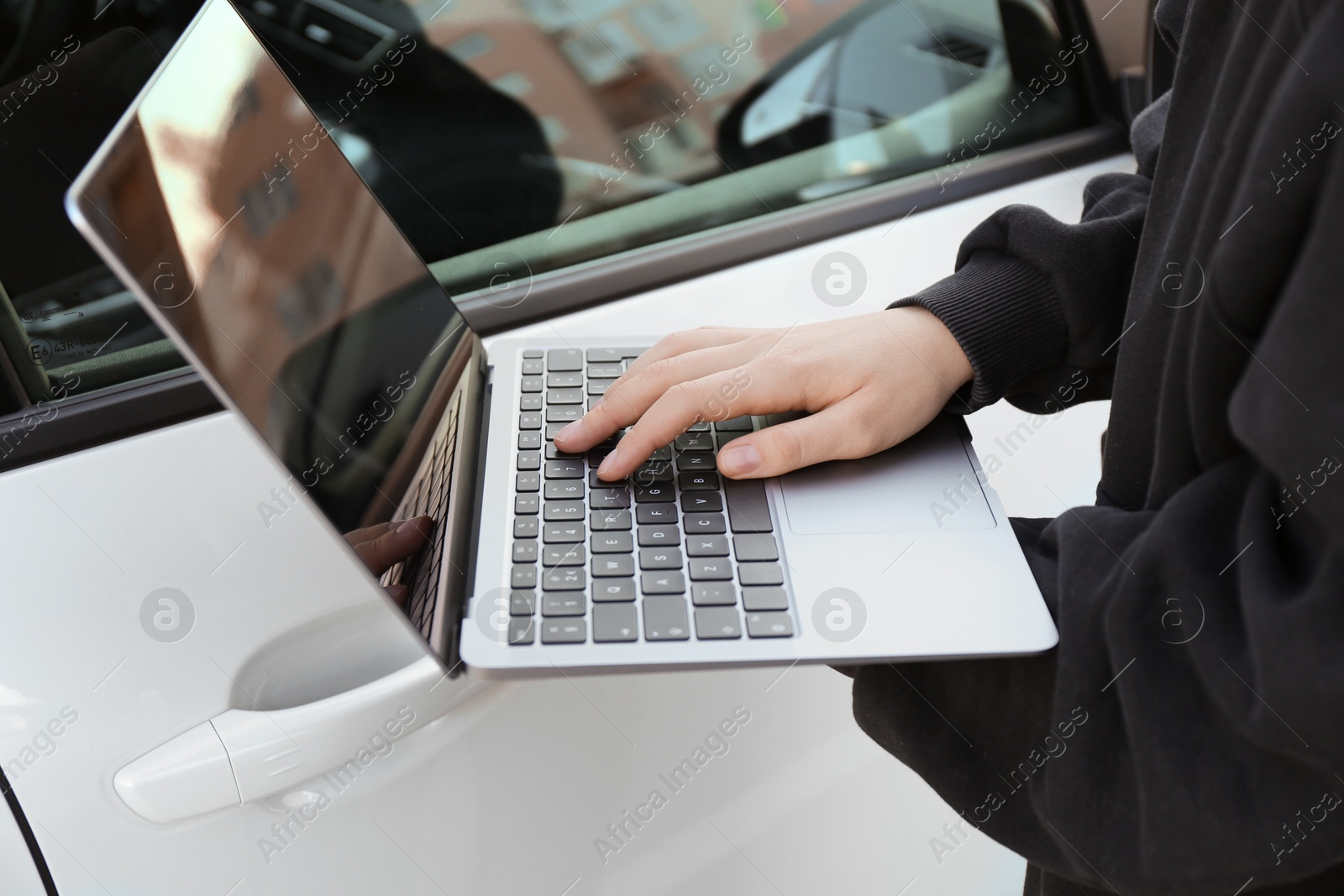 Photo of Thief hacking car system with laptop near vehicle, closeup