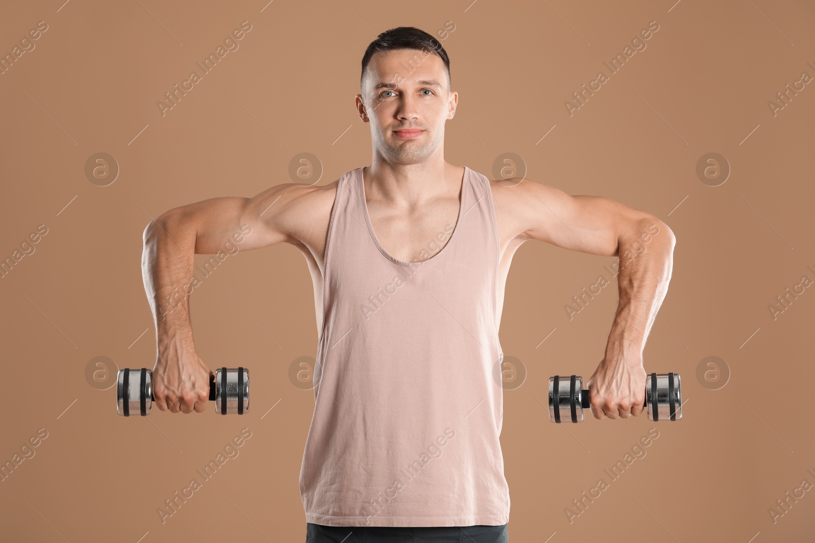 Photo of Man exercising with dumbbells on light brown background