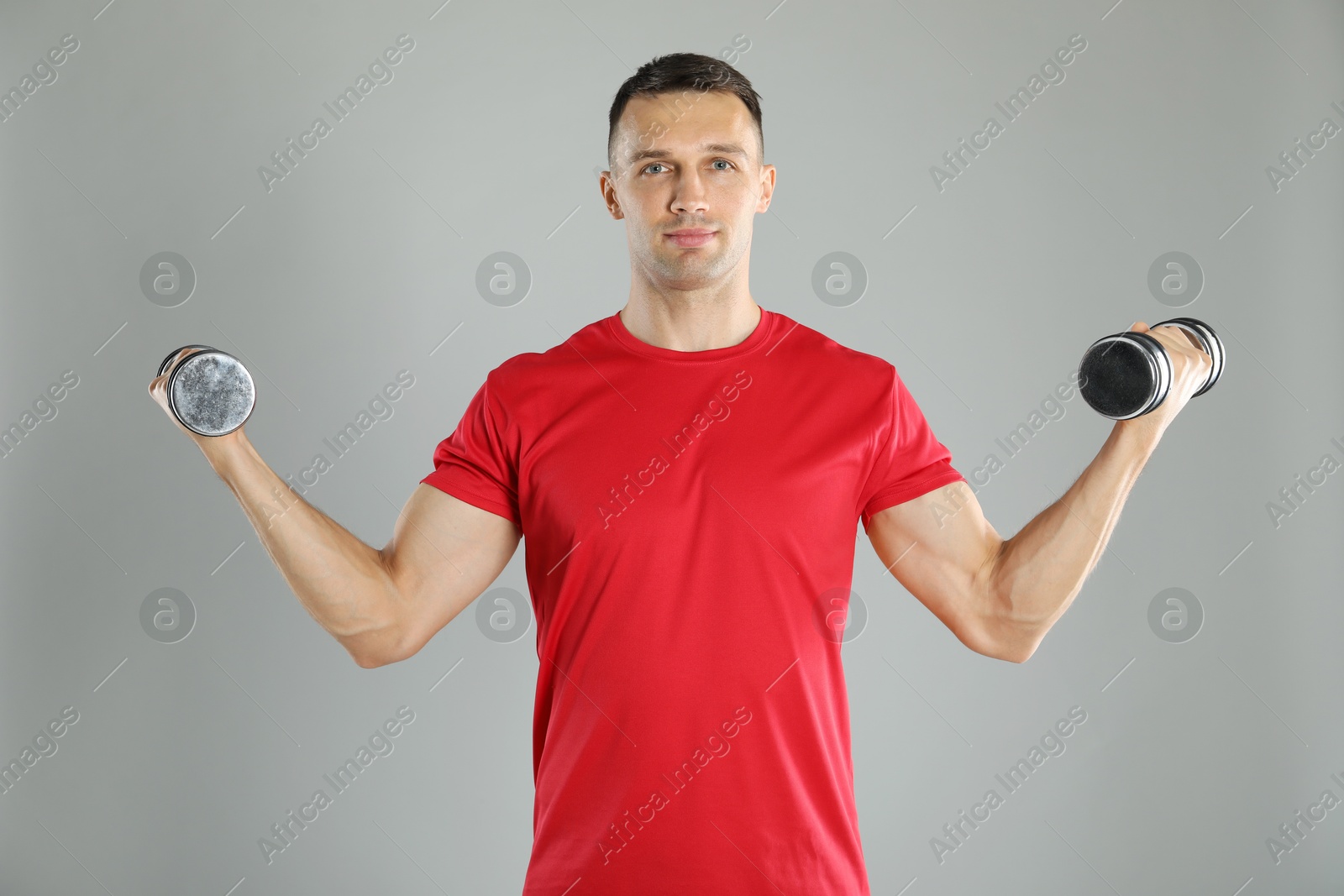 Photo of Man exercising with dumbbells on grey background