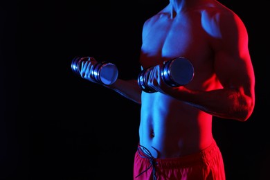 Photo of Man exercising with dumbbells in red light on black background, closeup. Space for text