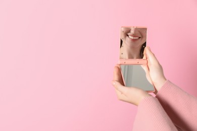 Photo of Woman with pocket mirror on pink background, closeup. Space for text