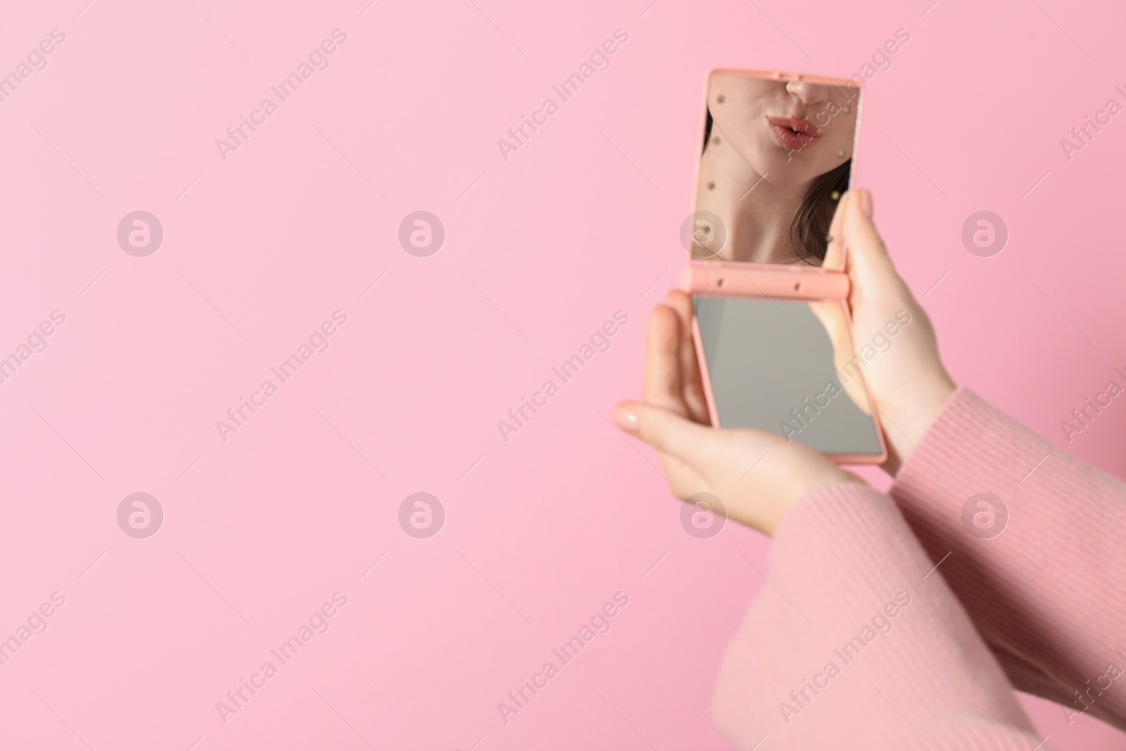 Photo of Woman holding pocket mirror on pink background, closeup. Space for text