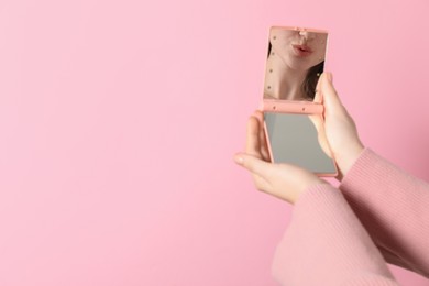 Woman holding pocket mirror on pink background, closeup. Space for text