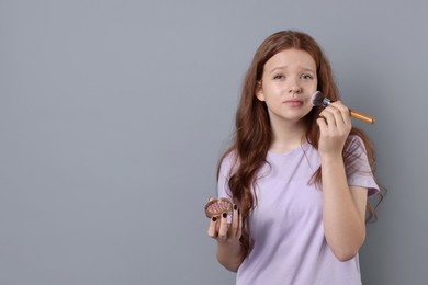 Photo of Teenage girl applying blush with brush on light grey background, space for text