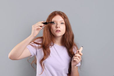 Photo of Teenage girl applying mascara on light grey background