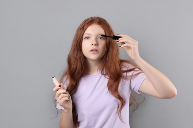 Teenage girl applying mascara on light grey background