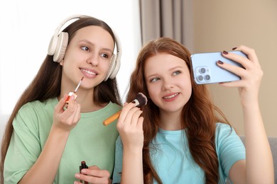 Teenage girls applying makeup products and taking selfie indoors