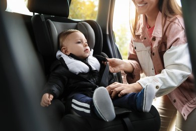 Photo of Smiling mother fastening her baby in car seat, closeup