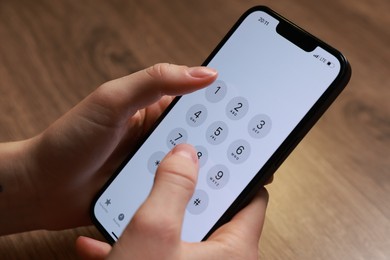 Photo of Woman dialing number on smartphone at wooden table, closeup