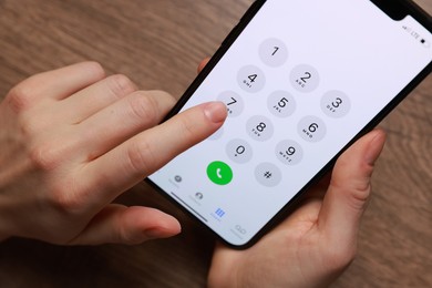 Photo of Woman dialing number on smartphone at wooden table, closeup