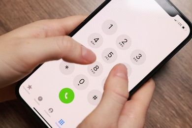 Photo of Woman dialing number on smartphone at wooden table, closeup