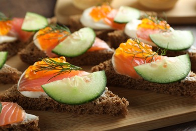 Photo of Tasty canapes with salmon and cucumber on wooden table, closeup