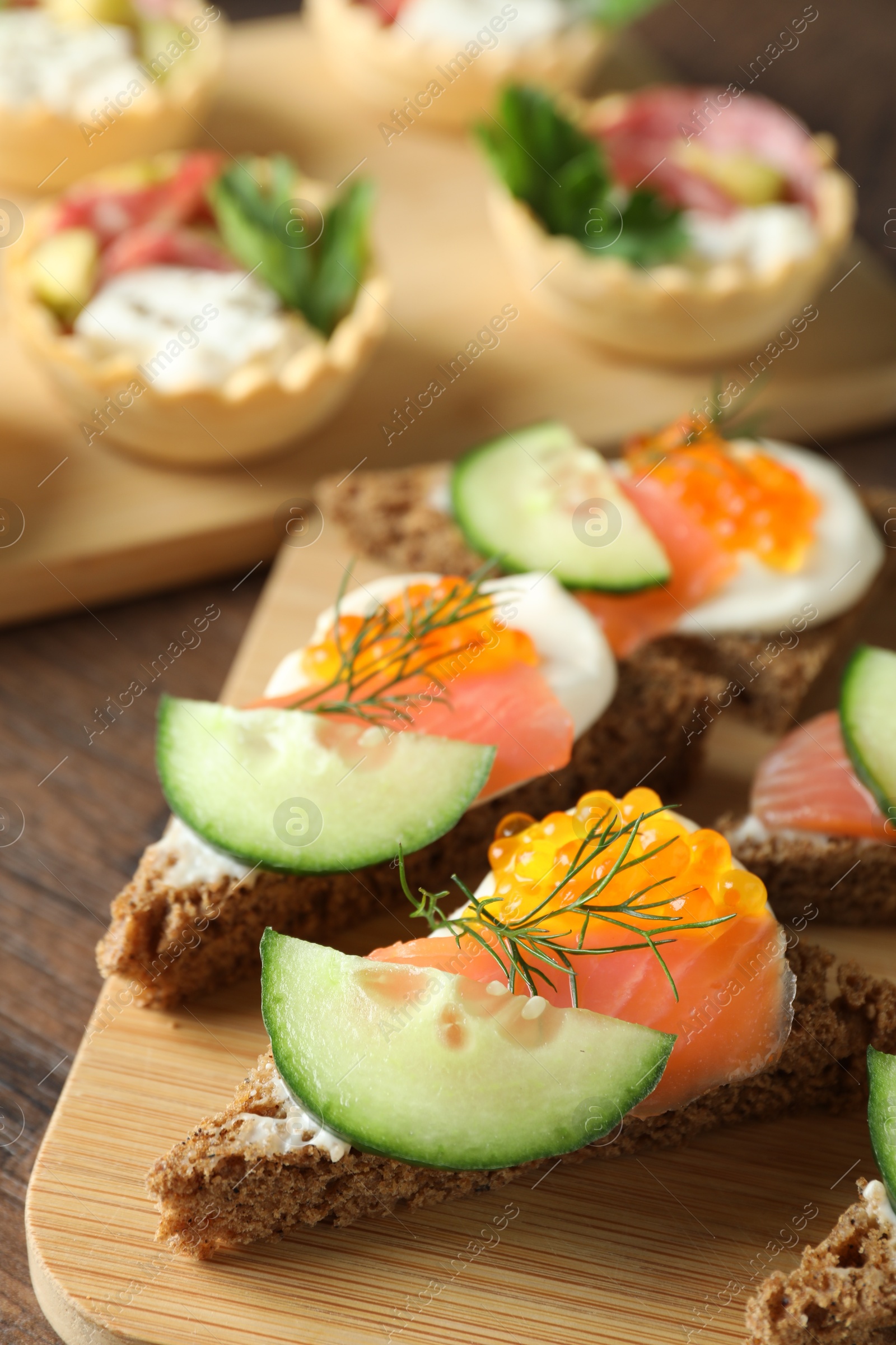 Photo of Tasty canapes with salmon and cucumber on wooden table, closeup