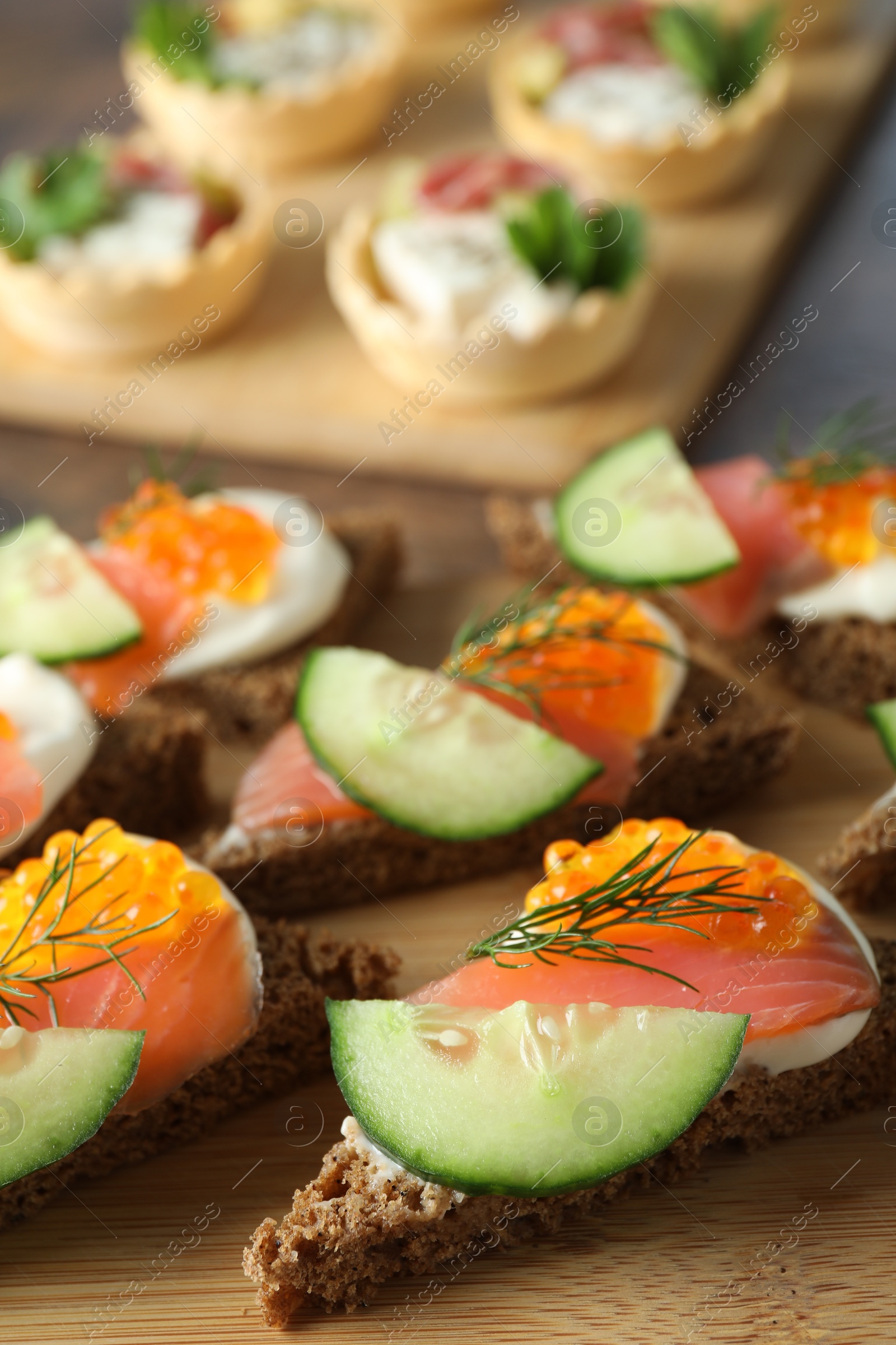 Photo of Tasty canapes with salmon and cucumber on wooden table, closeup